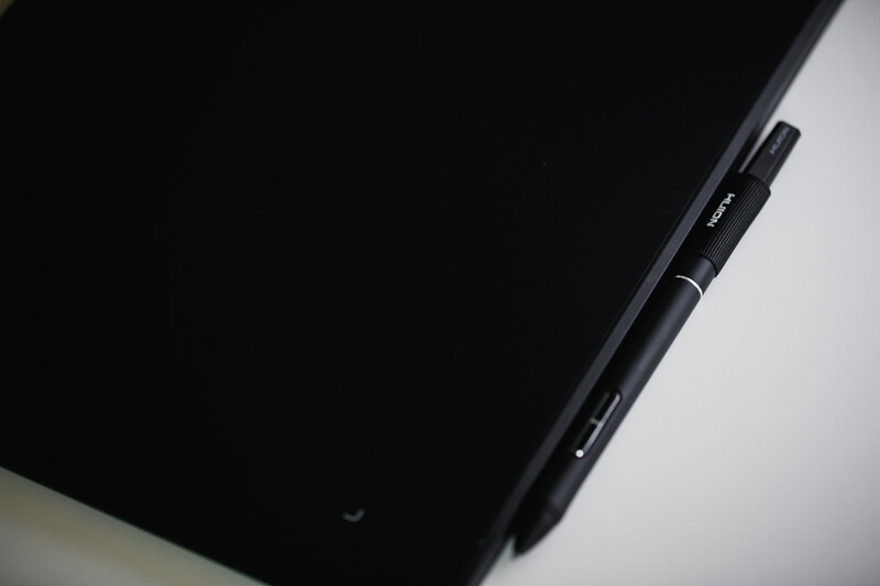 Black stylus pen resting on tablet device against white surface.