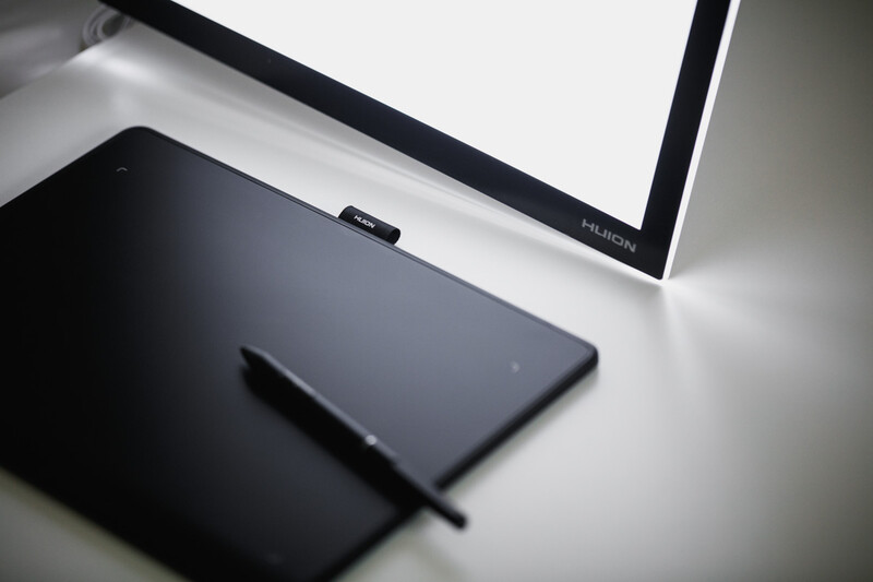 Graphics tablet with stylus pen positioned next to a computer monitor on a white desk setup.