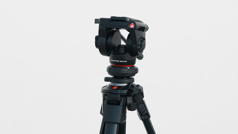 Professional fluid head video tripod with black pan-tilt head and three-stage legs against a neutral background.