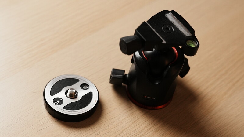 Ball head tripod mount with quick-release plate on wooden surface.