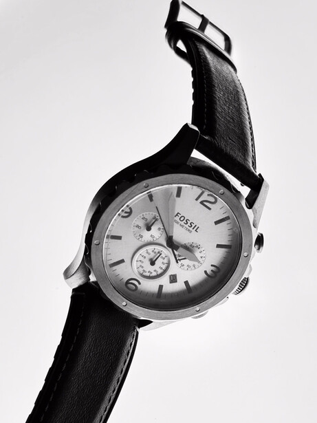 Chronograph wristwatch with dark leather strap against white background, shot at upward angle.