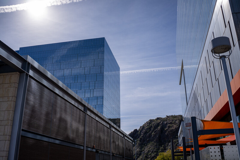 Modern blue-glass building with mountain backdrop under bright sunlight and clear sky.