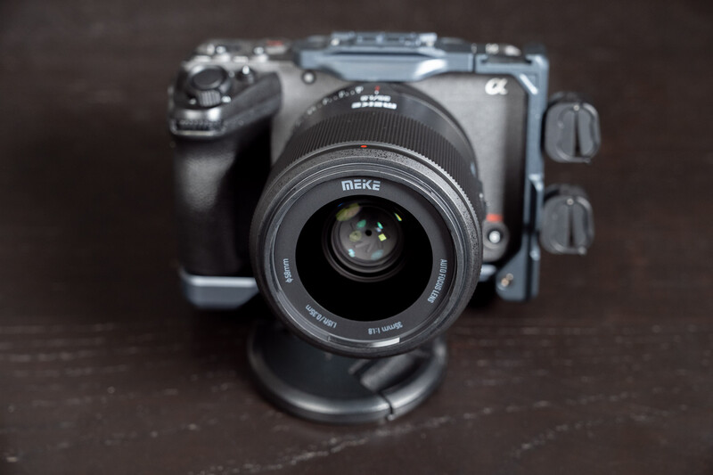 Meike lens mounted on mirrorless camera body with gimbal stabilizer on dark surface.
