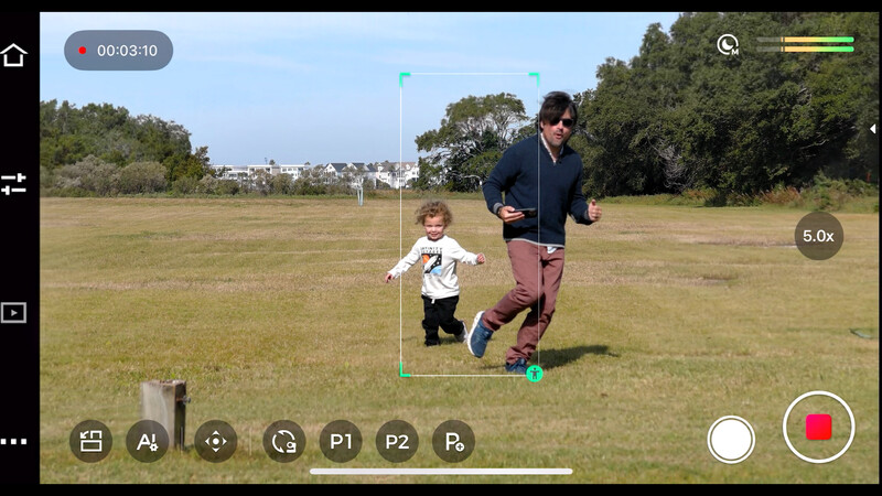 Screenshot of smartphone video interface showing an adult and toddler running in an open field.