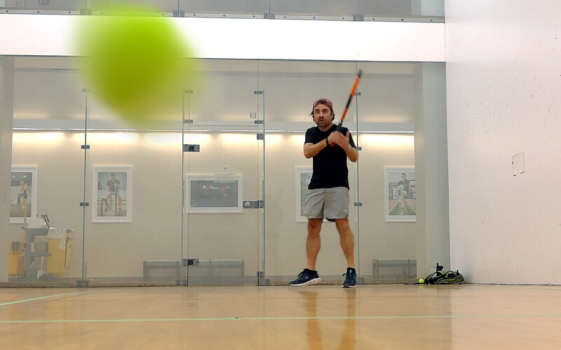Athlete in an indoor gymnasium taking a baseball swing at a green ball in mid-air.