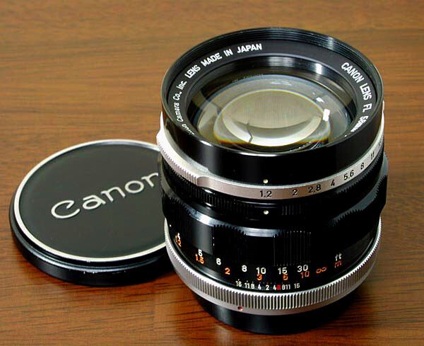 Canon rangefinder lens with black cap on wooden surface, showing aperture ring and focus scale.