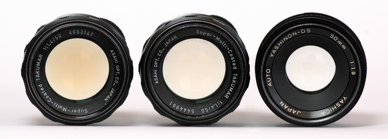 Three vintage camera lenses arranged side by side against a white background.
