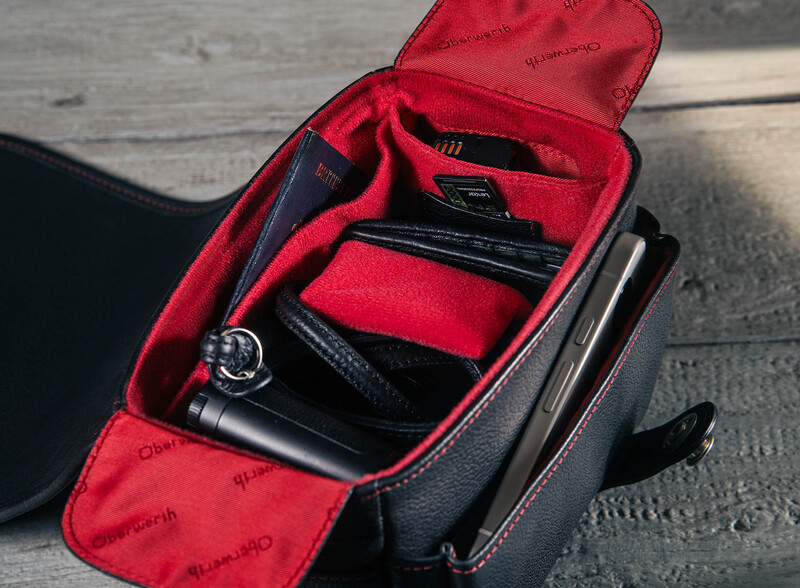 Open camera bag with red interior compartments displaying photography gear and accessories.