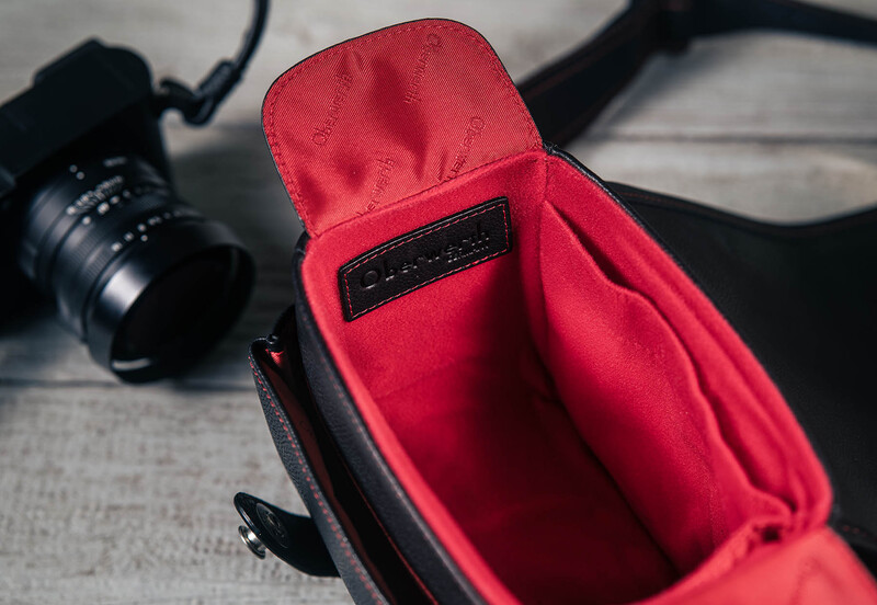 Red camera bag with open compartment displaying interior storage next to telephoto lens and camera body.