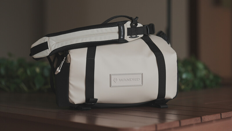 White and black camera bag with shoulder strap displayed on brick surface.