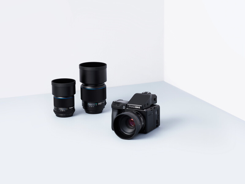 A compact mirrorless camera with two prime lenses arranged on a white surface.
