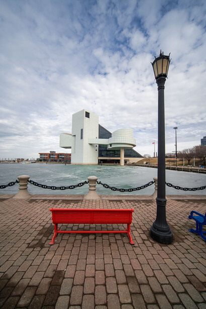 Red bench facing a modern waterfront building with curved white architecture under partly cloudy sky.