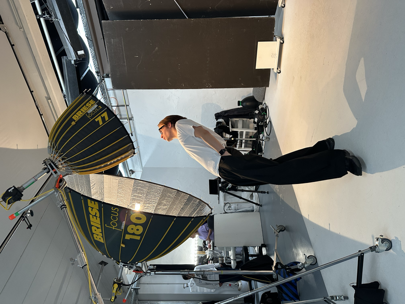 Overhead view of a photography studio setup with a model, reflector, and lighting equipment on a white seamless surface.