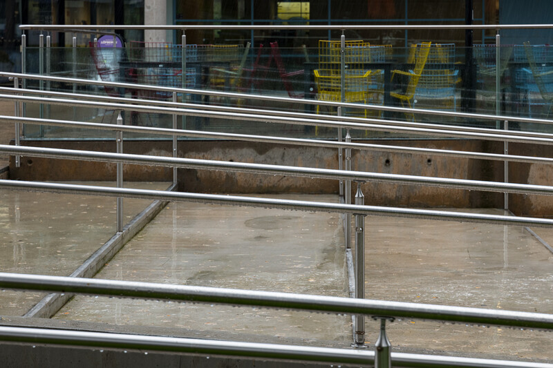 Metal railings and wet concrete surface with industrial building facade in background.