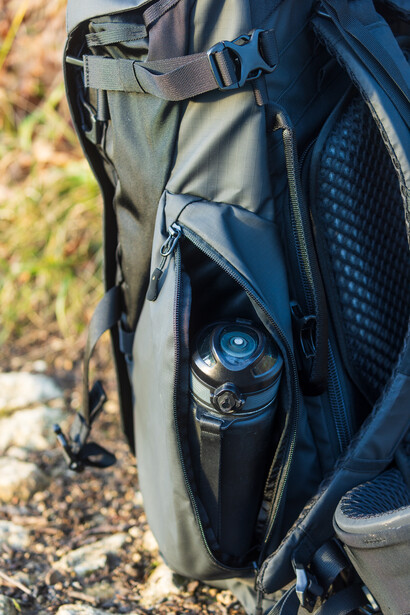 Camera gear packed in an open backpack pocket with a water bottle visible inside.