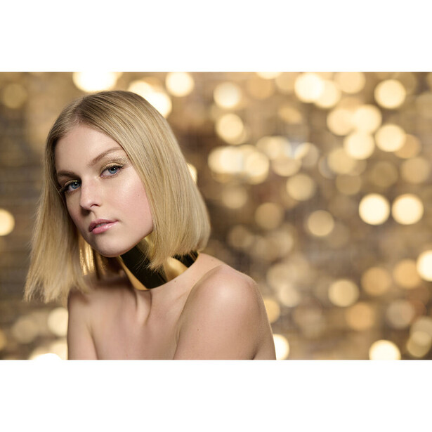 Woman with blonde bob haircut against soft golden bokeh background.