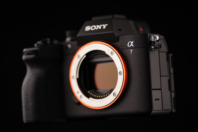 Sony a7 mirrorless camera body with orange-highlighted lens mount against black background.