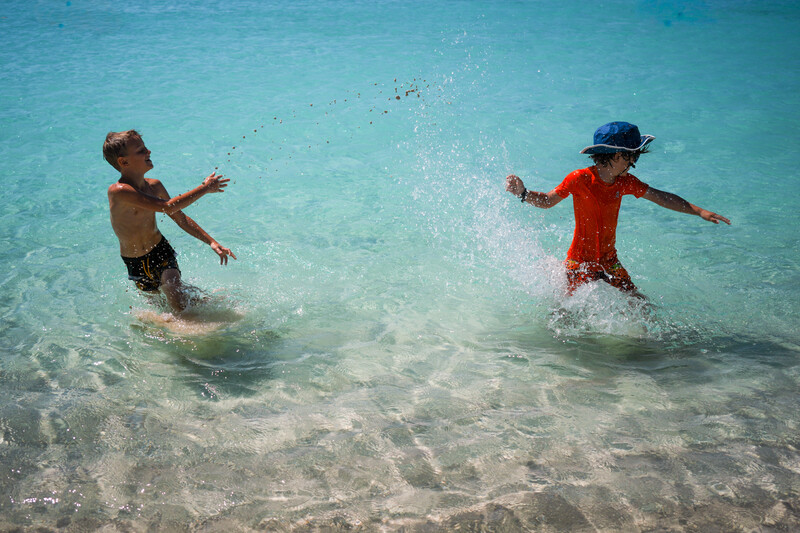 Two children running through shallow turquoise water with arms outstretched, splashing in the surf.
