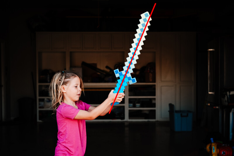 Child in pink shirt holding toy sword with blue and red details indoors.