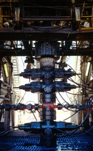 Industrial machinery with blue hydraulic cylinders arranged symmetrically, photographed from below looking upward through metal framework.