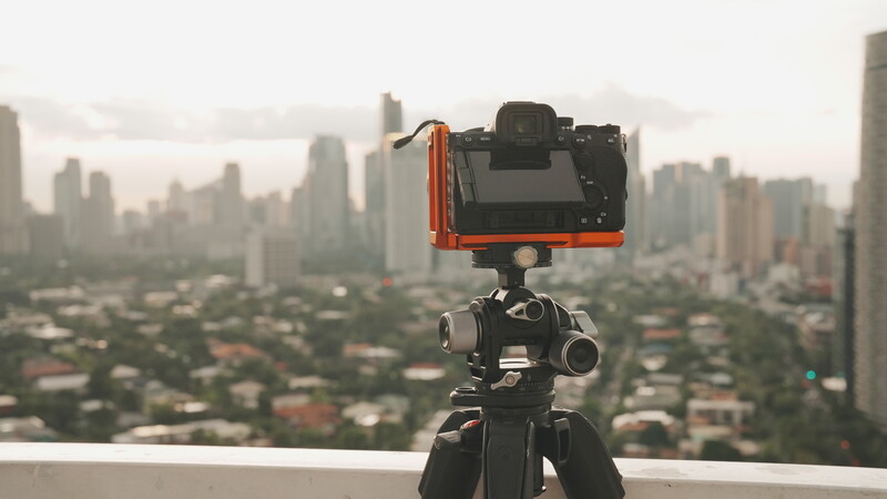 Mirrorless camera mounted on tripod with cityscape backdrop, shot from elevated vantage point overlooking urban sprawl.
