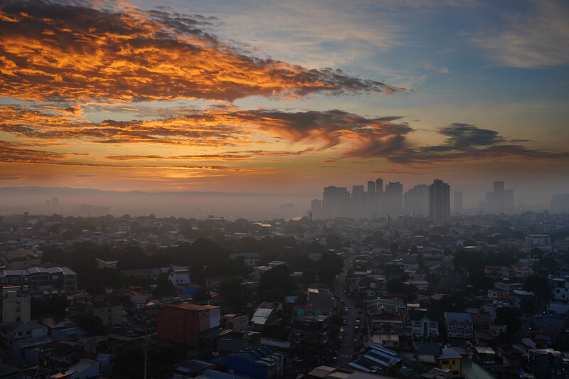 Urban skyline silhouetted against dramatic golden and orange clouds at sunset.