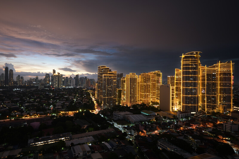 Illuminated high-rise buildings frame a twilight cityscape with dramatic purple-blue storm clouds overhead.