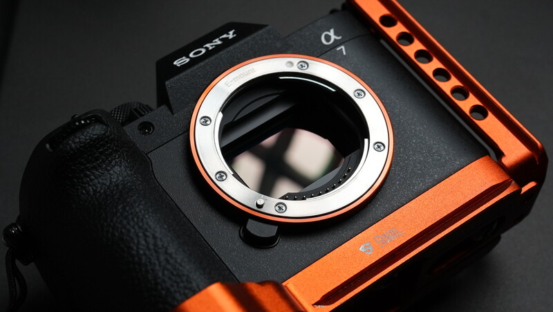 Sony mirrorless camera with black body and orange accents, showing open lens mount and interior mirror mechanism.
