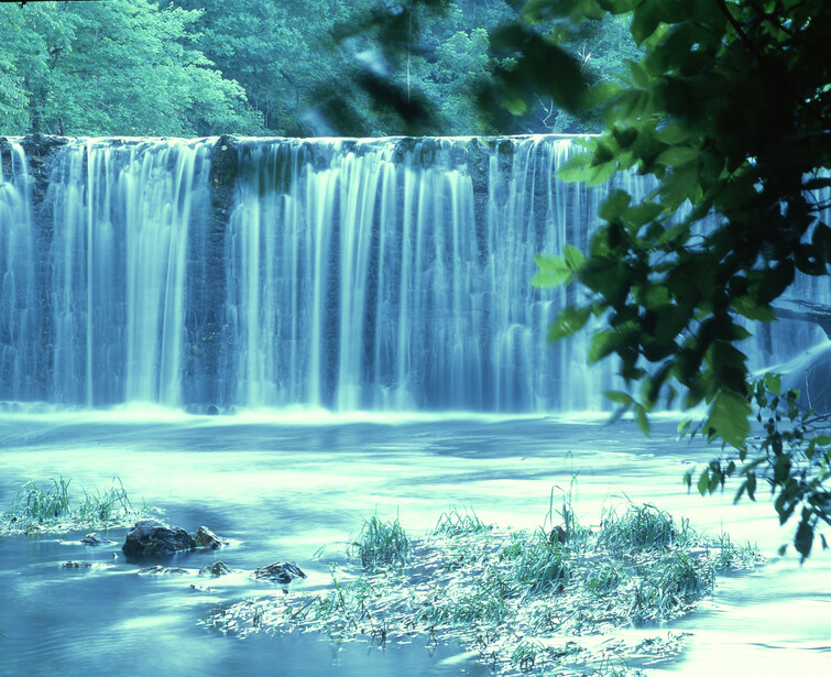 Waterfall with multiple vertical streams flowing into a turquoise pool surrounded by lush vegetation.