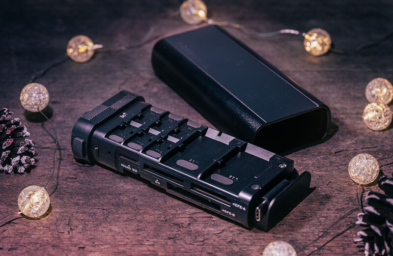 Black audio interface with control knobs and faders next to smartphone on textured surface.
