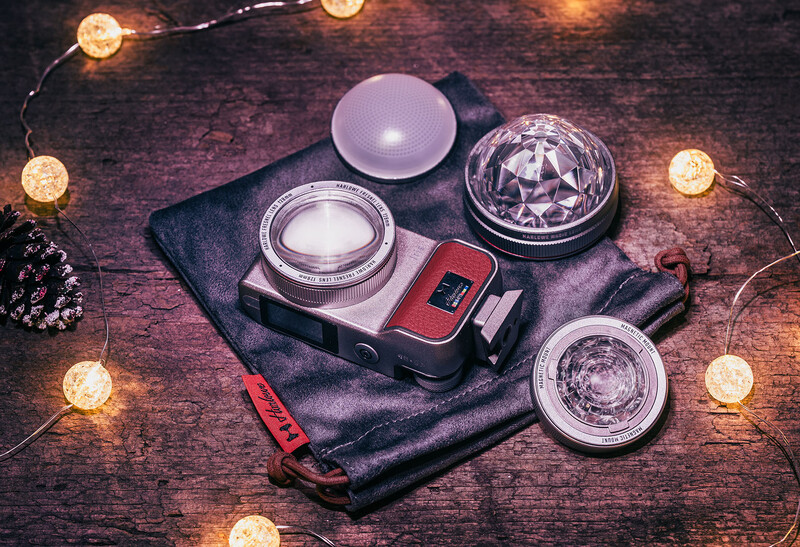 Photography accessories and lens filters arranged on a black cloth with warm string lights surrounding them.