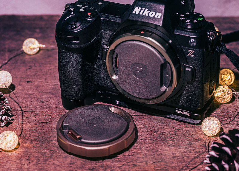 Nikon Z mirrorless camera body with lens cap and body cap on pink textured surface surrounded by decorative elements.