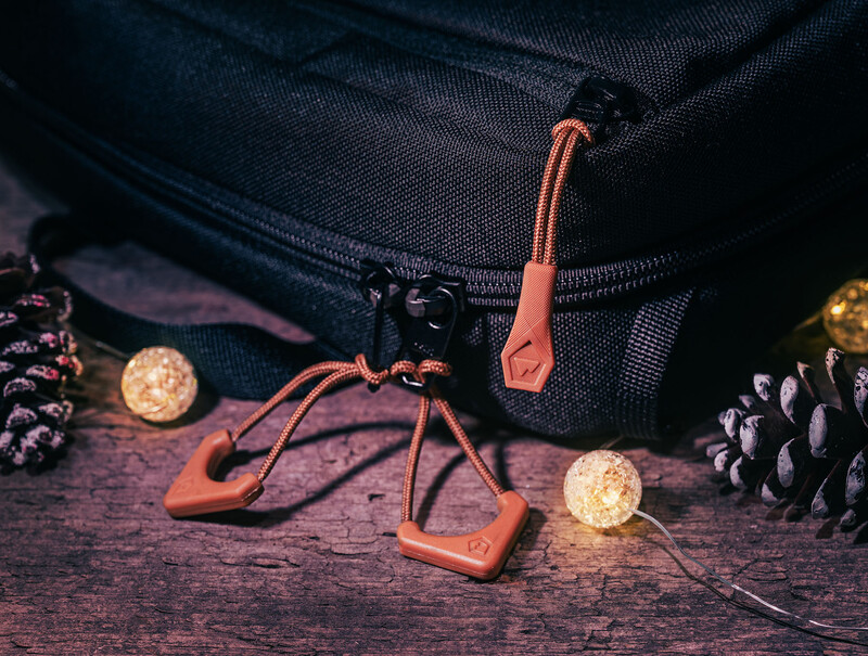 Orange climbing quickdraws and carabiners arranged on wooden surface with pinecones and glowing orbs.