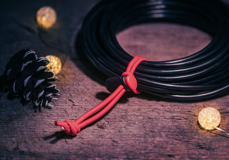 Red cord with knots tied in it, coiled black cable, pinecone, and warm glowing orbs arranged on textured wood surface.
