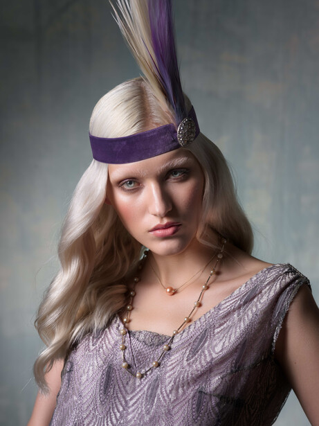Woman wearing purple headband and beaded dress against neutral gray background.
