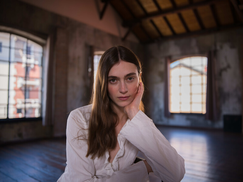 Woman in white shirt posing in industrial loft space with hand to face.