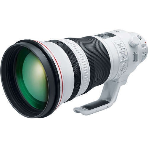 White telephoto lens with green-tinted glass elements and focus ring, displayed against white background.