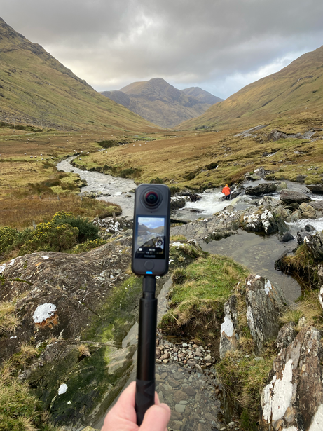 Smartphone mounted on a tripod capturing a mountain valley landscape with a flowing stream.