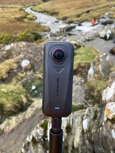 360-degree camera mounted on a tripod overlooking a rocky mountain stream landscape.