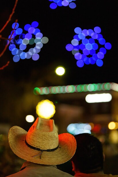 Miniature sombrero balanced on a wooden railing with bokeh lights in background.