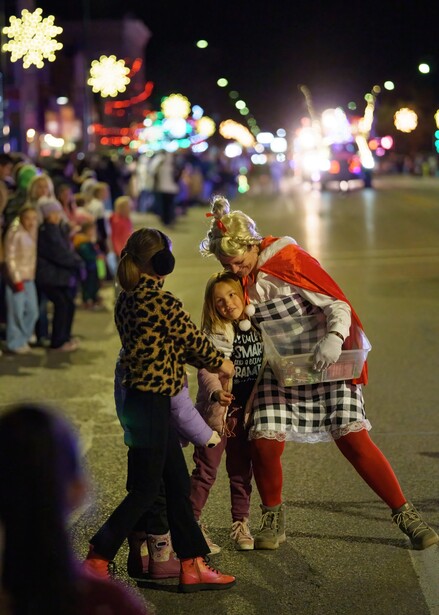 Children in festive costumes dancing together at an outdoor evening event with blurred carnival lights in the background.