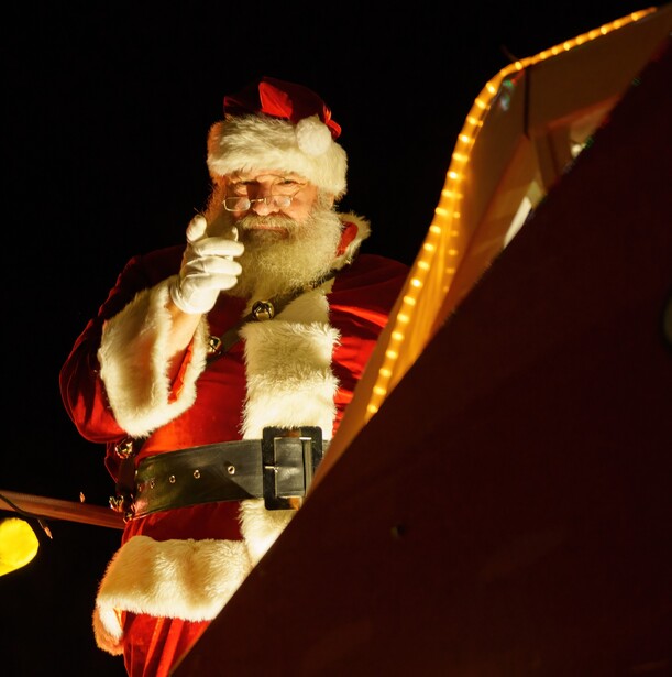 Illuminated Santa Claus figure against a black night sky, waving with a gold-outlined sleigh visible to the right.