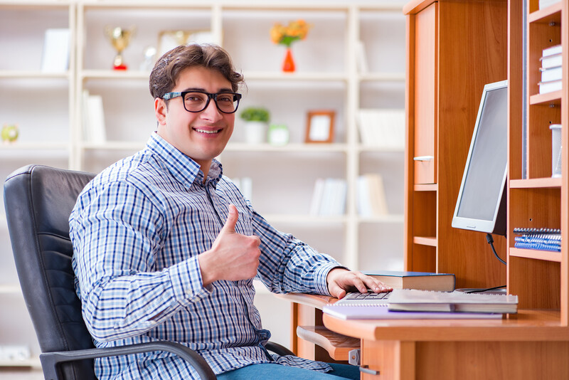 Man in checkered shirt at desk giving thumbs up while working at computer.