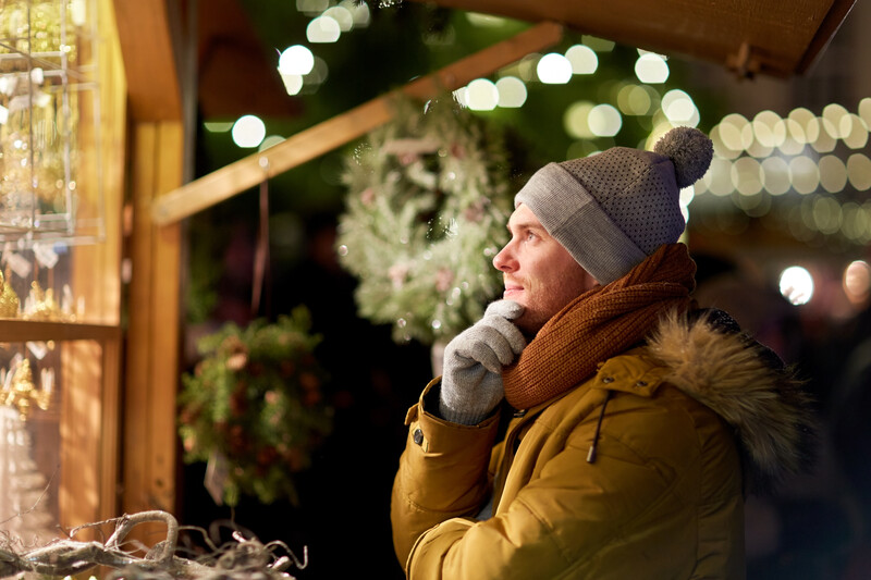 Man in yellow jacket and knit beanie gazing at holiday window display at night.