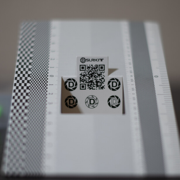 QR code test pattern with various QR code designs and logos on white paper with checkered border.