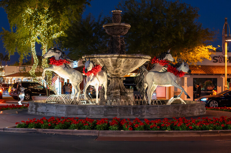 Illuminated elephant fountain decorated with red and white garland at dusk in a town plaza.