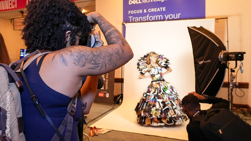 Photographer shooting a fashion dress made from colorful magazine clippings on a white seamless backdrop.