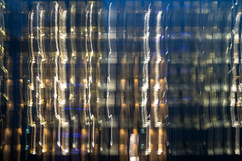 Vertical streaks of light and architectural elements create an abstract, motion-blurred urban composition.