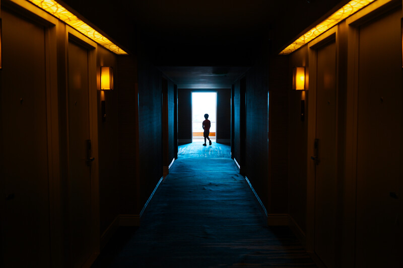 Silhouetted figure standing at the bright end of a dark corridor with warm and cool lighting contrast.