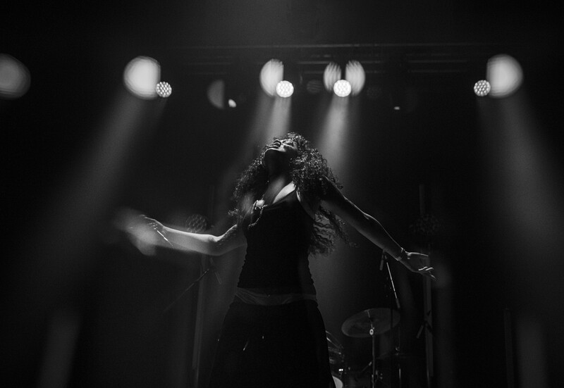 Singer performing on stage with dramatic backlighting and atmospheric stage lights in black and white.